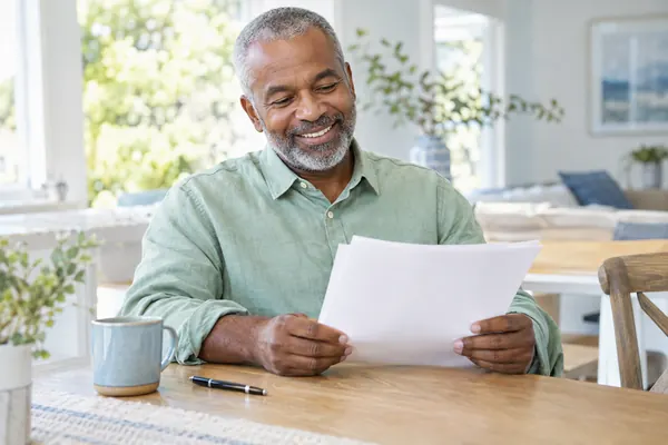 Smiling older man at a sunlit kitchen table reading the pages of his signed promissory note